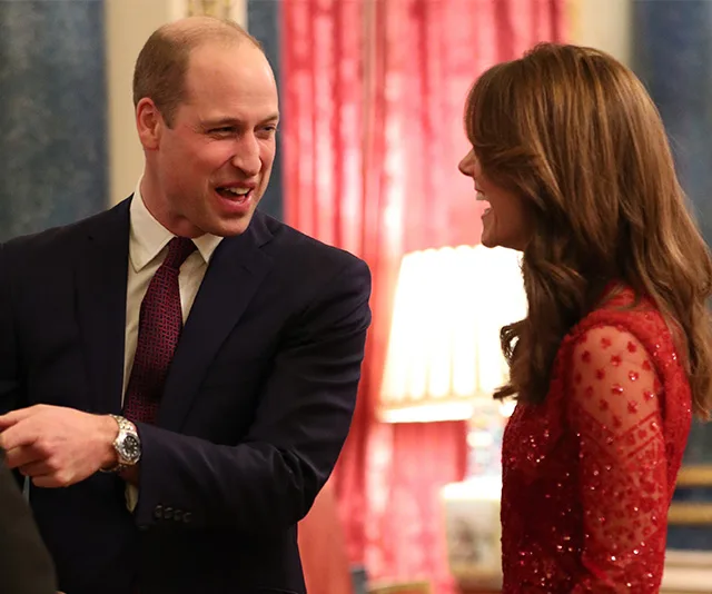 Two people smiling and conversing at a formal event; one wears a red sparkly dress, the other a suit.