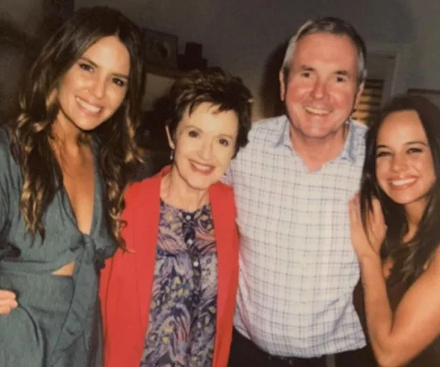 Group photo with four smiling individuals, including a woman in a red jacket, likely from a social gathering.