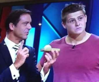 Two men stand on a TV game show set; one holds a check.