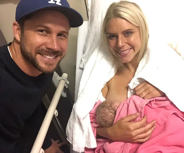 Man and woman smiling with newborn baby wrapped in pink blanket at hospital.