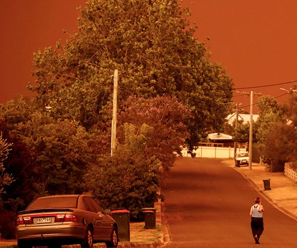 A person walks down a street under an orange sky during bushfires in Mallacoota, with trees lining the road.