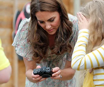 Kate Middleton bends over to show a camera to a young girl covering her face.