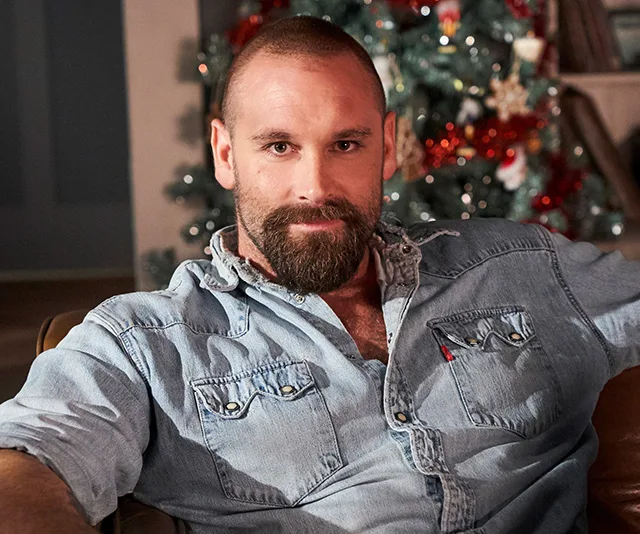 Man in a denim shirt sitting, with a Christmas tree in the background.