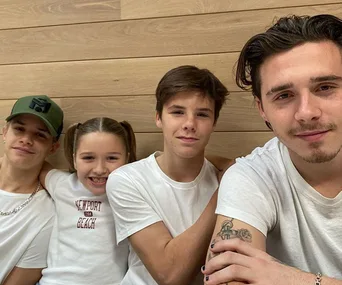 Four youths smiling and sitting close together, one with a tattoo visible on their arm.