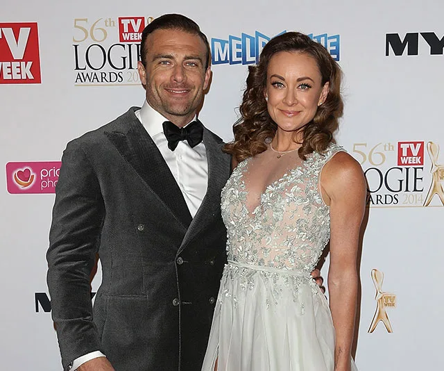 Pair posing at the Logie Awards 2014 red carpet, man in tuxedo, woman in an embellished gown, backdrop with logos.