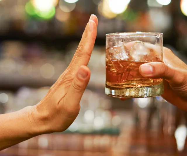 A hand rejecting an offered glass of alcohol in a bar setting.