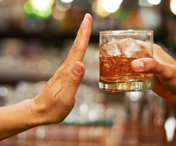 A hand rejecting an offered glass of alcohol in a bar setting.