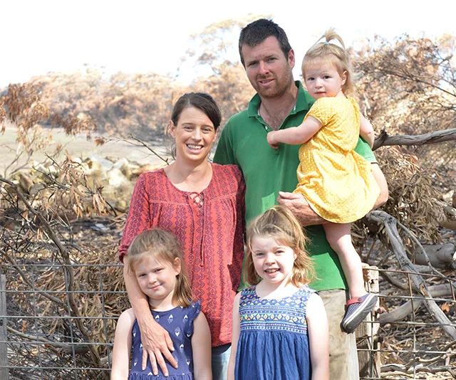 Family standing together in front of bushland affected by fires, smiling at the camera.