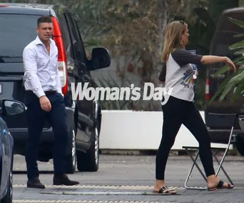 A man in a white shirt and a woman in casual outfit are walking outside near parked cars.