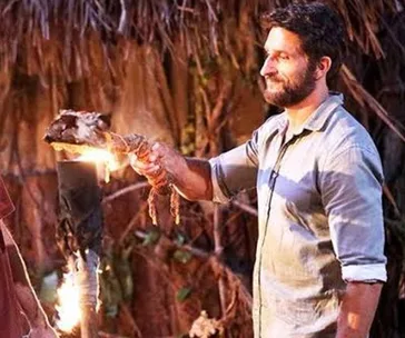 Man in a blue shirt extinguishing a torch on "Australian Survivor: All Stars" tribal council set.