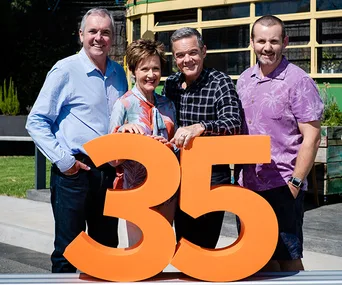 Group of four people standing behind a large orange number 35, indicating a celebration or anniversary.