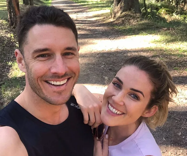 A couple taking a smiling selfie on a forest path during a sunny day.