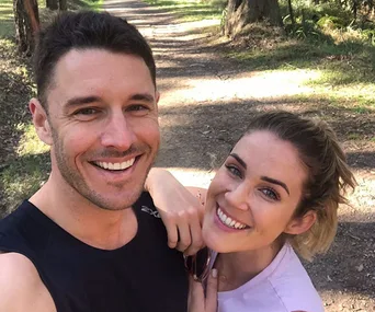 A couple taking a smiling selfie on a forest path during a sunny day.