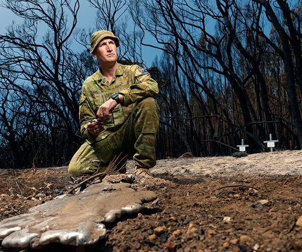 Australian soldier kneels on burned ground amid charred trees on Kangaroo Island after bushfires.
