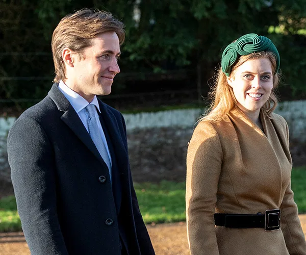 A couple walking outdoors, dressed formally; the woman wears a green headband, and the man is in a coat and tie.
