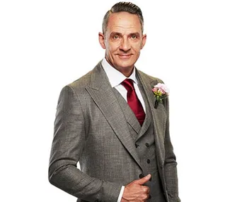 Man in gray suit, red tie, flower boutonniere, smiling with hand in pocket against white background.