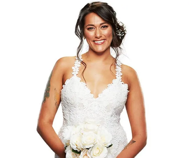 Bride in a white lace gown holding a bouquet, smiling, with dark hair styled in an updo.