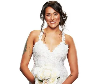 Bride in a white lace gown holding a bouquet, smiling, with dark hair styled in an updo.