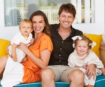 Family sitting together on a couch, smiling at the camera with two young children.