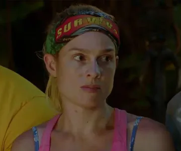 Woman wearing a "Survivor" headband, looking serious, in a jungle setting from a reality TV show episode.