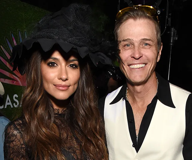 A woman in a black lace outfit and wide-brimmed hat stands beside a smiling man in a white and black shirt.