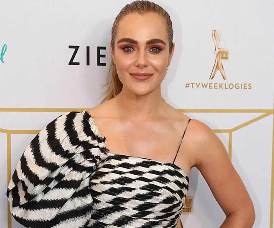 A woman in a black and white patterned dress at a TV award event, standing before a logo backdrop.