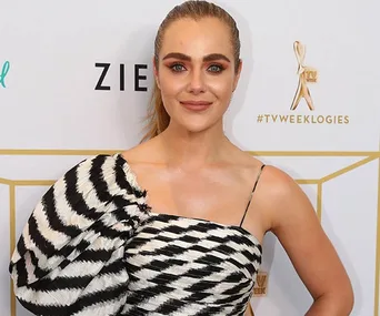A woman in a black and white patterned dress at a TV award event, standing before a logo backdrop.