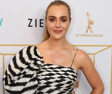 A woman in a black and white patterned dress at a TV award event, standing before a logo backdrop.