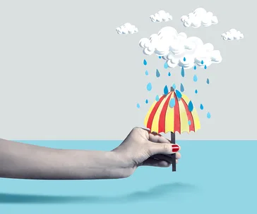 A hand holding a small red and yellow umbrella under illustrated clouds with raindrops against a blue and gray background.