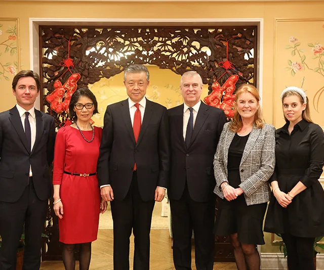 Group photo of six people, including individuals in formal attire, standing together in an ornately decorated room.