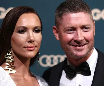 Two individuals in formal attire pose together at an event; a woman with long earrings and a man in a black bow tie.
