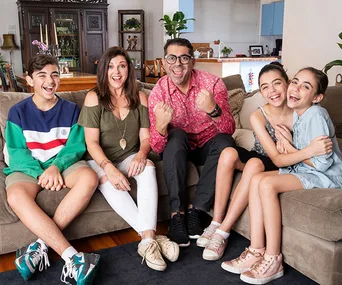 A family of five sitting on a couch, smiling and cheering in a living room setting.