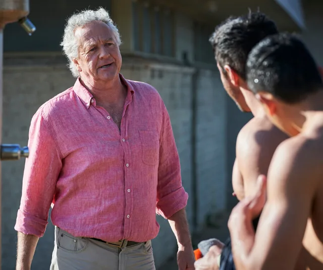 Man in pink shirt talks to two men at an outdoor location on a sunny day.