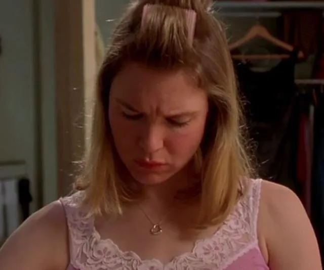 A woman with blonde hair in a pink camisole looks down, appearing concerned or focused indoors.