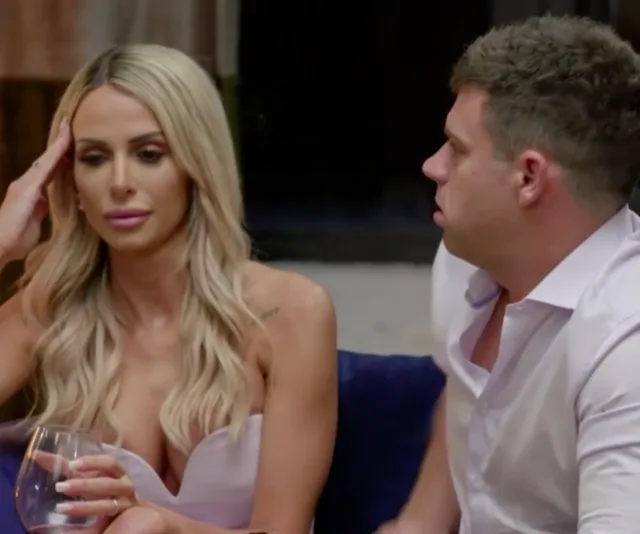 A woman and man sit together on a couch, appearing deep in conversation. The woman holds a glass.