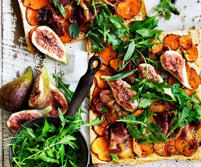 Flatbread topped with figs, sweet potatoes, prosciutto, and arugula on rustic table.