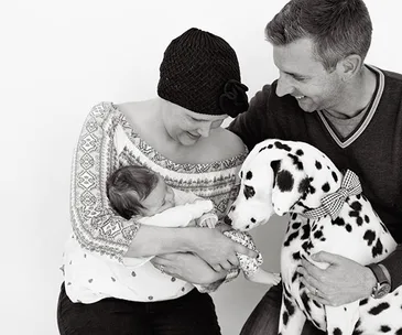 A couple looks lovingly at a newborn baby and a Dalmatian dog, creating a warm family moment.