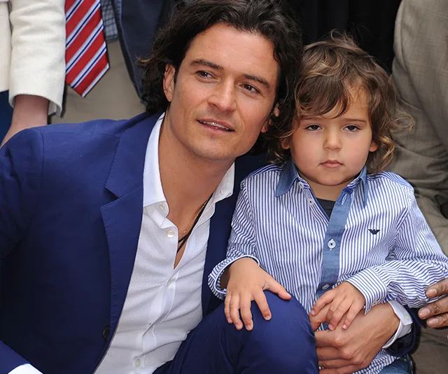 Man in a blue suit holding a young child in a striped shirt, both looking forward.