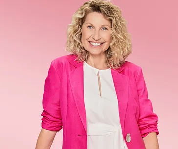 Woman smiling in bright pink jacket and white blouse against a pink background.
