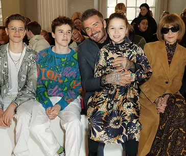 Family and fashion icon sit together at a fashion event, showcasing stylish outfits and vibrant atmosphere.