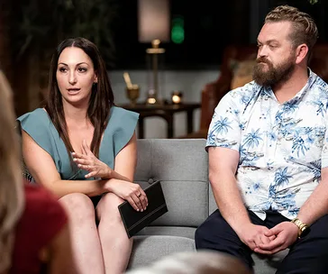 Two people seated on a couch during a discussion, with one gesturing while speaking.