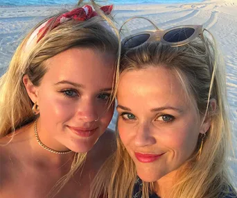 Mother and daughter smiling at the beach during sunset.