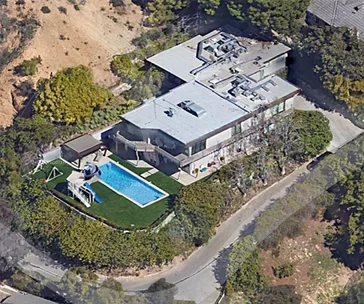 Aerial view of a modern house with a pool, surrounded by greenery in a hilly area.