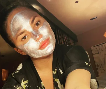 A person wearing a shimmering silver face mask, relaxing in a dimly lit room.