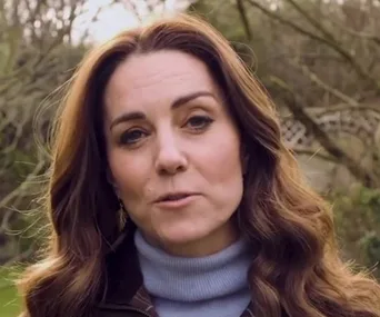 A woman with long brown hair speaking outdoors in a garden setting.