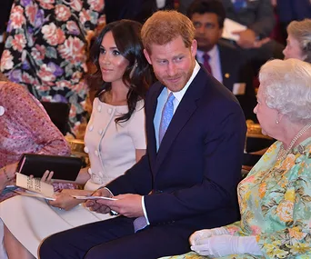 Prince Harry and Meghan Markle seated with the Queen at a formal event, holding programs.