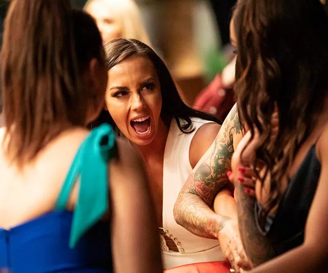 Woman in white dress shouting during an intense group discussion with others at a social event.