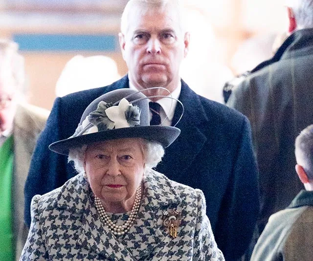 Senior woman in checked coat and hat with man in suit behind her in a crowded setting.
