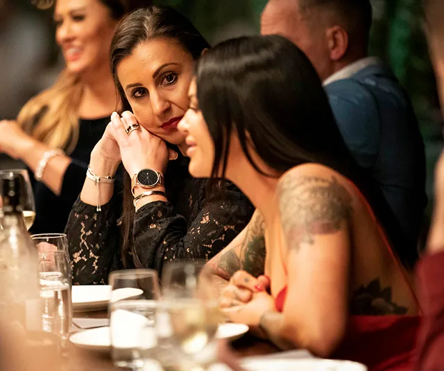 A group of people sit at a dinner table, engaging in conversation and sharing a meal.