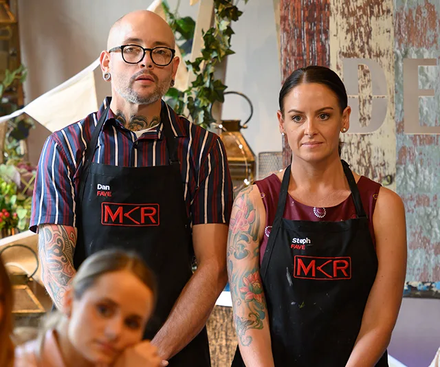 Dan and Steph from "My Kitchen Rules" in aprons, standing together, looking serious.